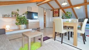 A modern living room with a TV, wooden beams, a dining area with chairs, and a green rug. - House 1044 (Svetvincenat)