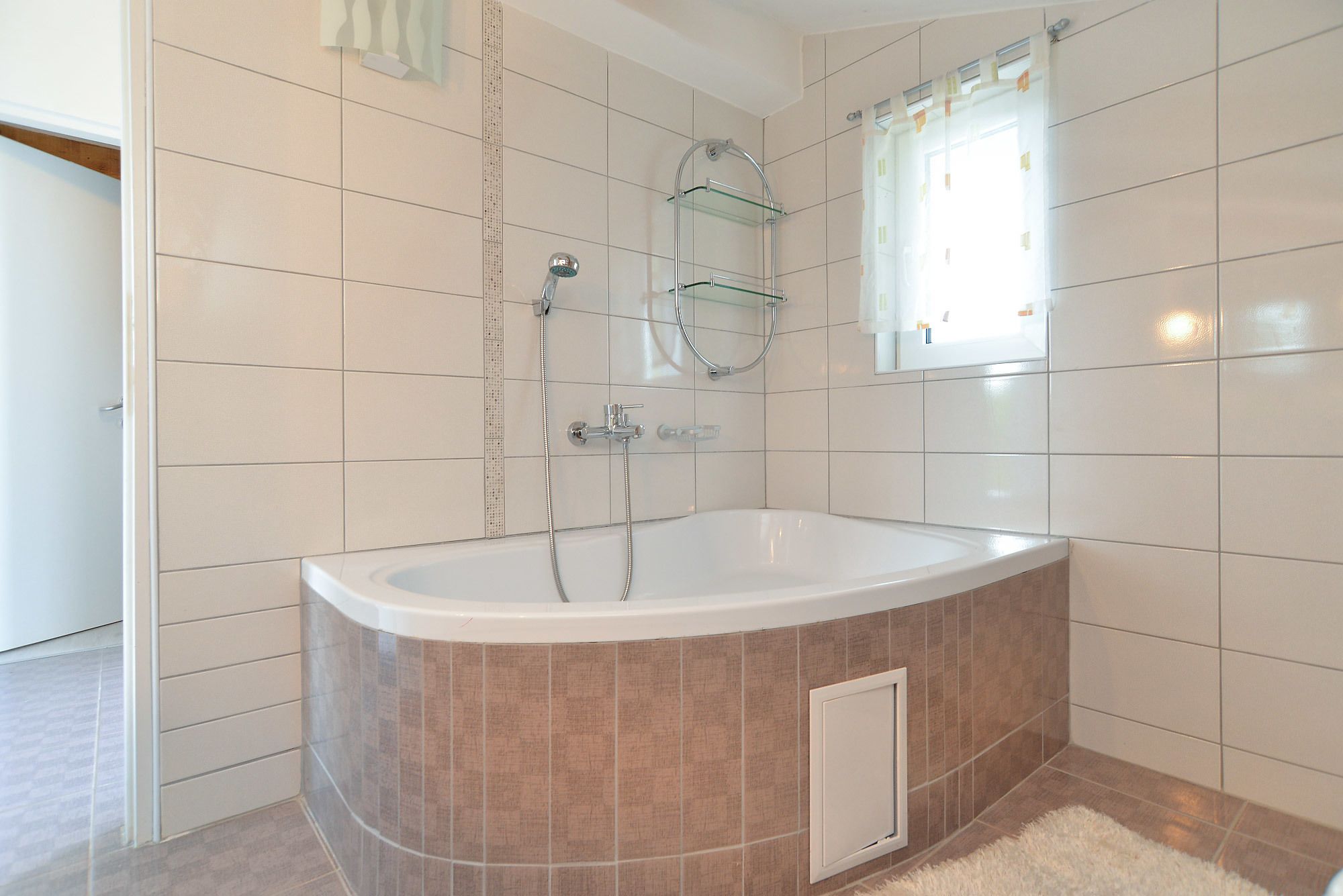 Ein modernes Badezimmer mit einer freistehenden Badewanne, einer Glasablage und einem Fenster mit Vorhängen.