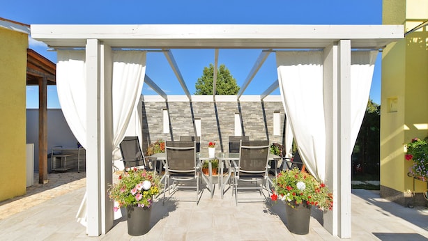 A covered outdoor patio with a table and chairs, surrounded by potted plants. - House 1044 (Svetvincenat)