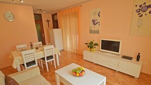 Un soggiorno con zona pranzo, televisore e una ciotola di frutta su un tavolino.