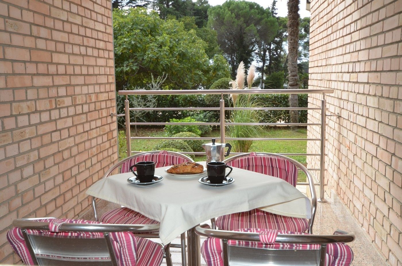 Eine Terrasse mit Tisch, gedeckt für zwei Personen, mit gestreiften Kissen und einer weißen Tischdecke.