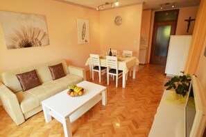 Una sala de estar con un sofá, una mesa de comedor para dos personas y una mesa de centro blanca con fruta.