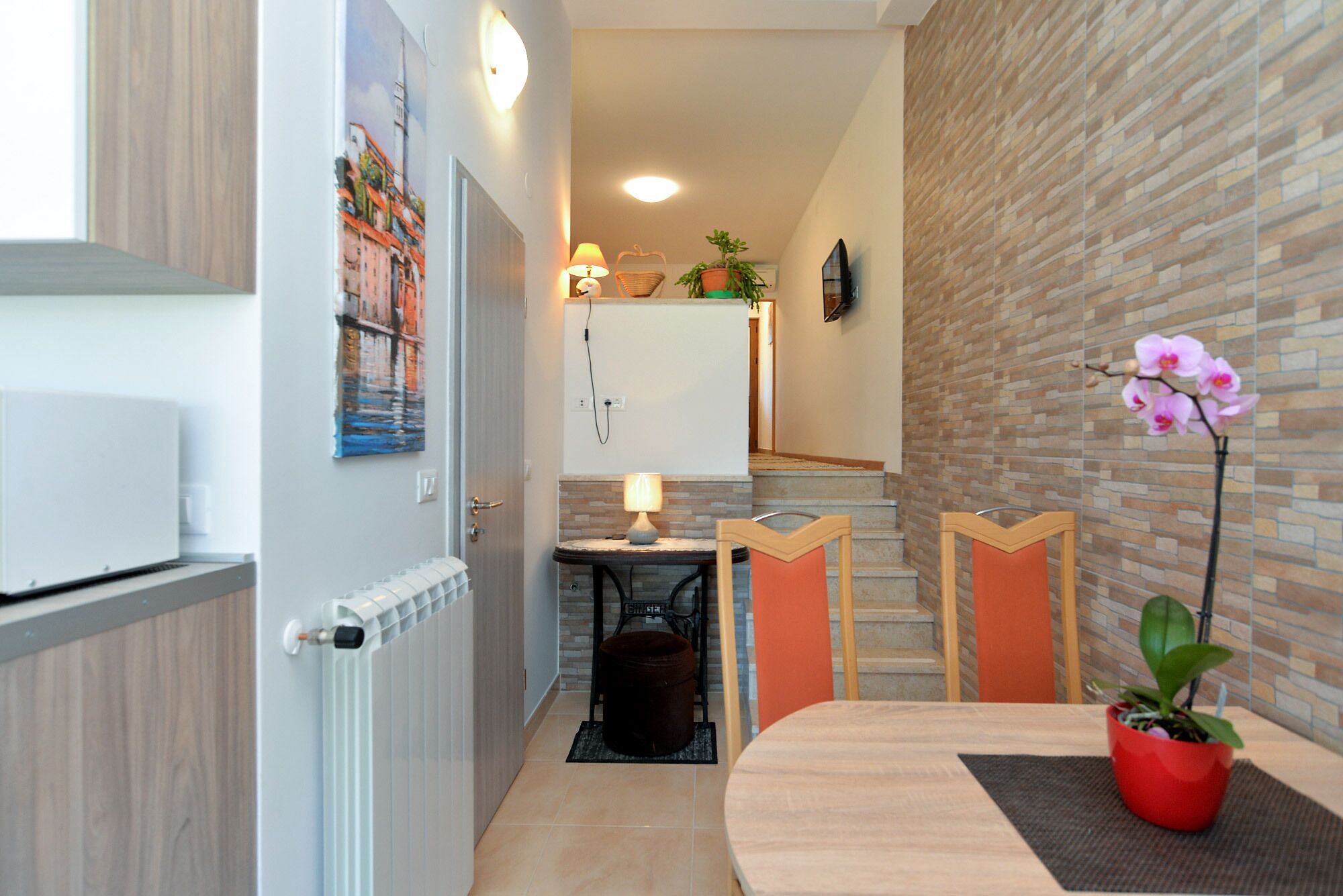Una cocina moderna con un refrigerador blanco, un comedor con mesa y sillas de madera, y una pared de ladrillo con una orquídea en maceta.