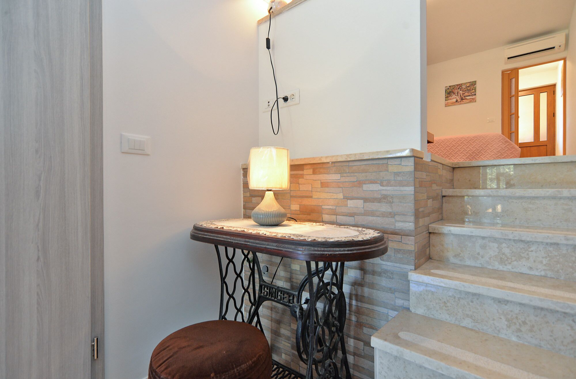 Un escalier avec des marches en pierre et une rampe, une petite table avec une lampe et un banc marron.