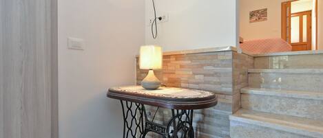 Un escalier avec des marches en pierre et une rampe, une petite table avec une lampe et un banc marron.