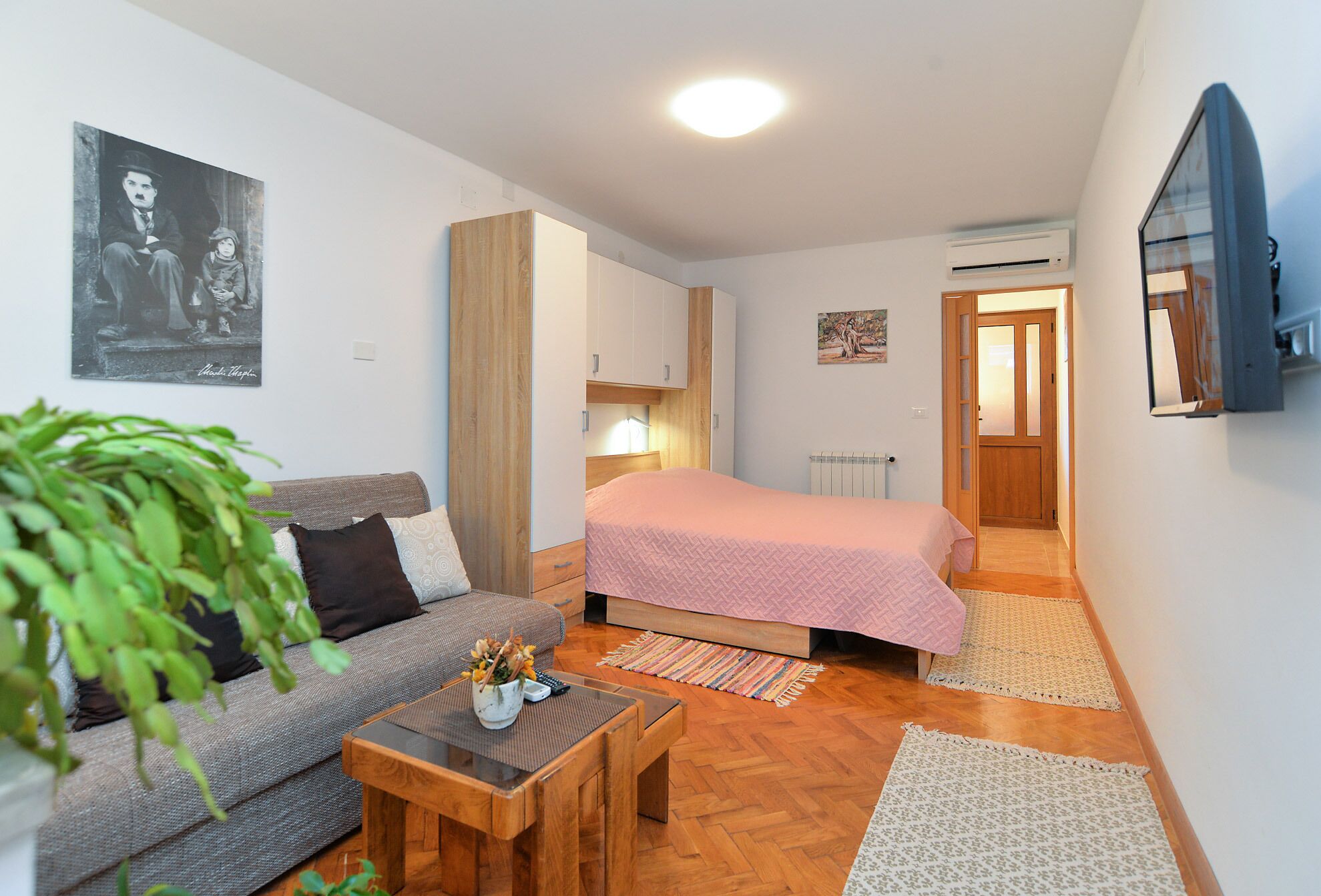 A compact bedroom with a bed, a sofa, a small table, and a potted plant.