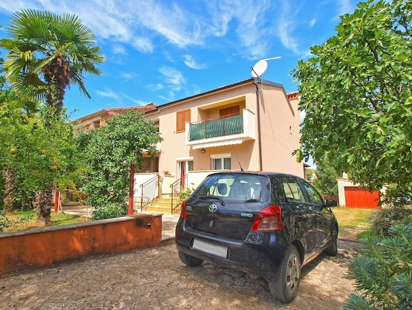 A black car parked in front of a building with a satellite dish, surrounded by greenery and a clear sky.
