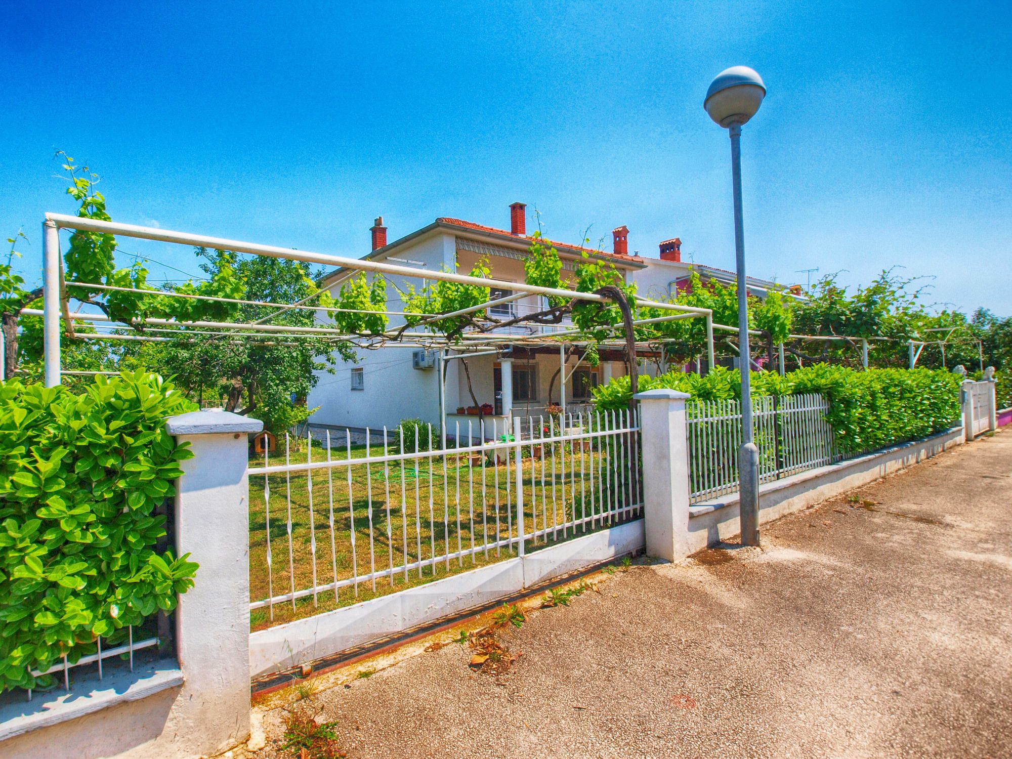 A residential property with a white fence, a street lamp, and a clear blue sky.