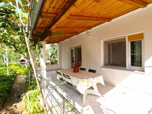 An outdoor patio with a table and chairs, surrounded by greenery and a wooden pergola.