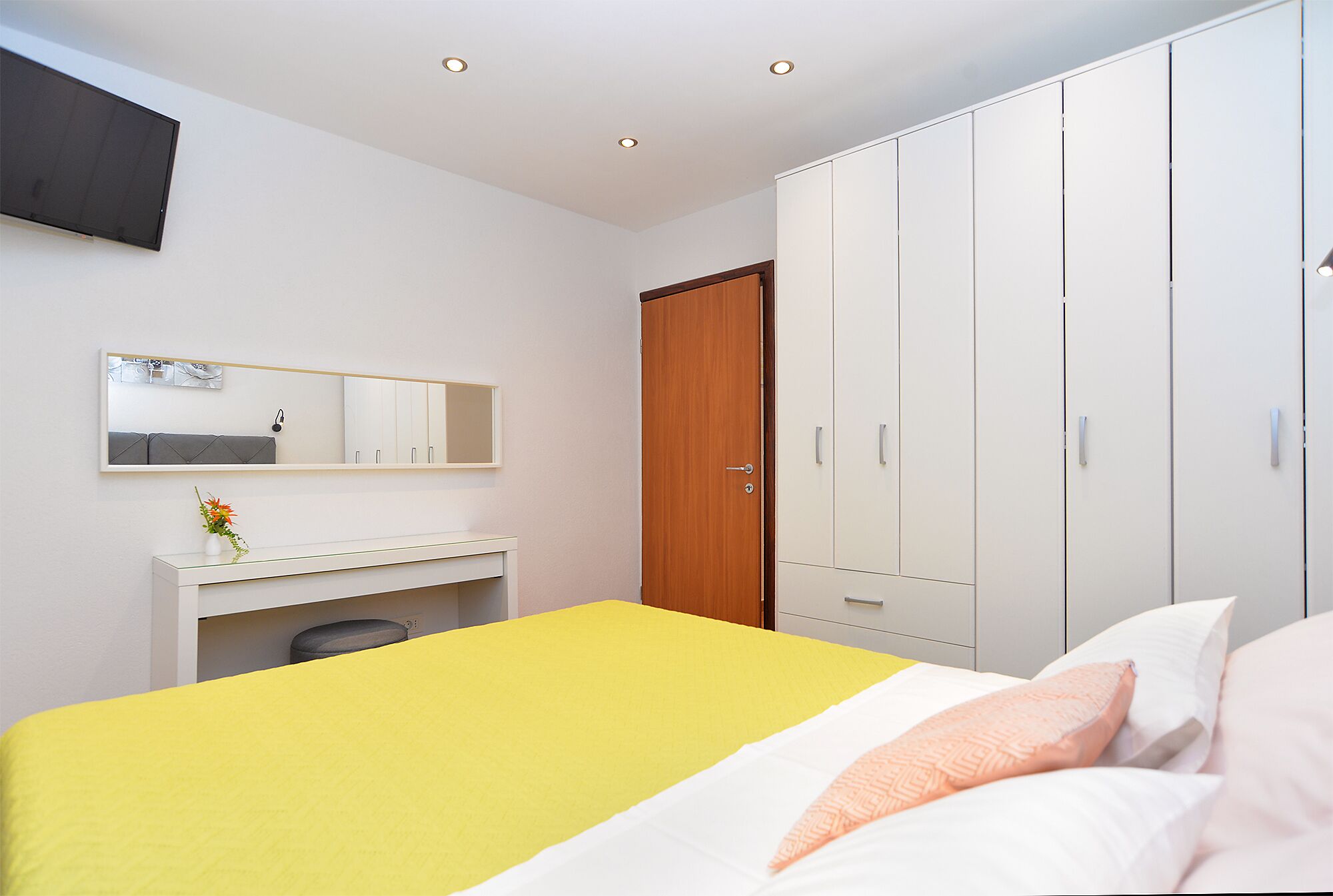 A bedroom with a bed, a wardrobe, a desk, and a mirror.