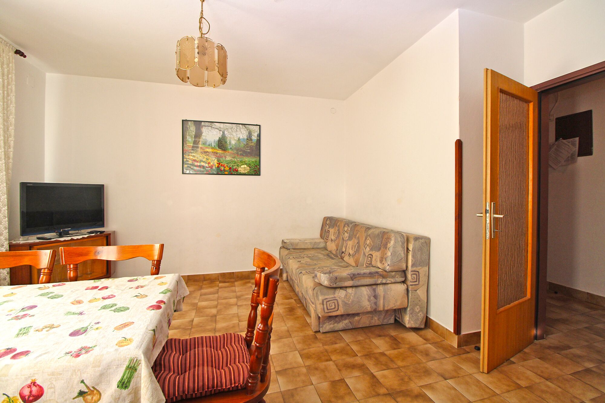 A room with a dining table, chairs, a sofa, a television, and a door.