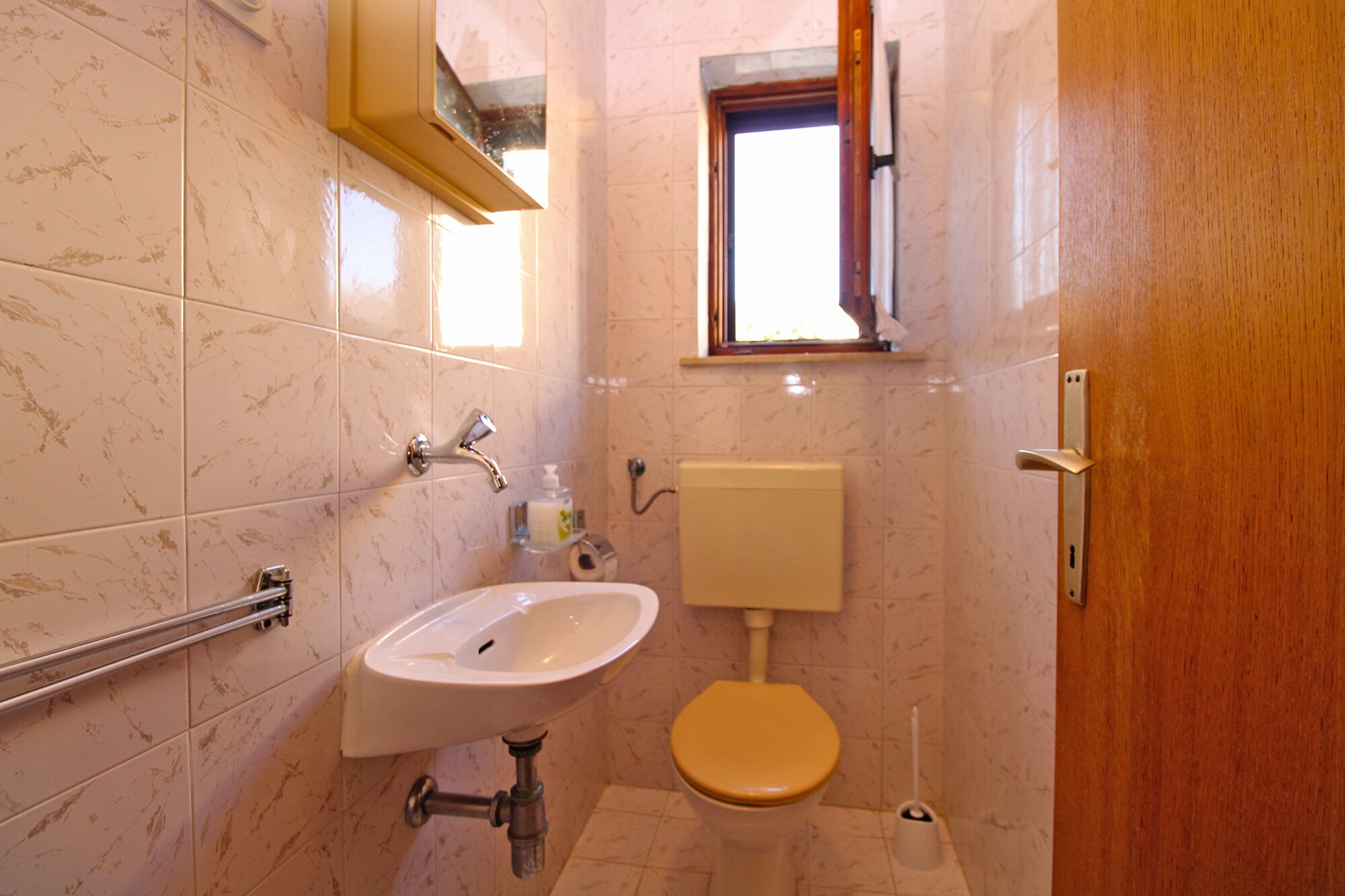 Une salle de bain avec un lavabo blanc, des toilettes et une fenêtre située au-dessus des toilettes.