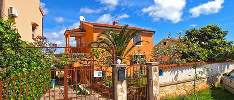 A gated entrance with a stone wall, a palm tree, and a building with a red roof.