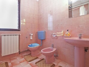 A bathroom with pink tiles, a toilet, bidet, sink, and a radiator.