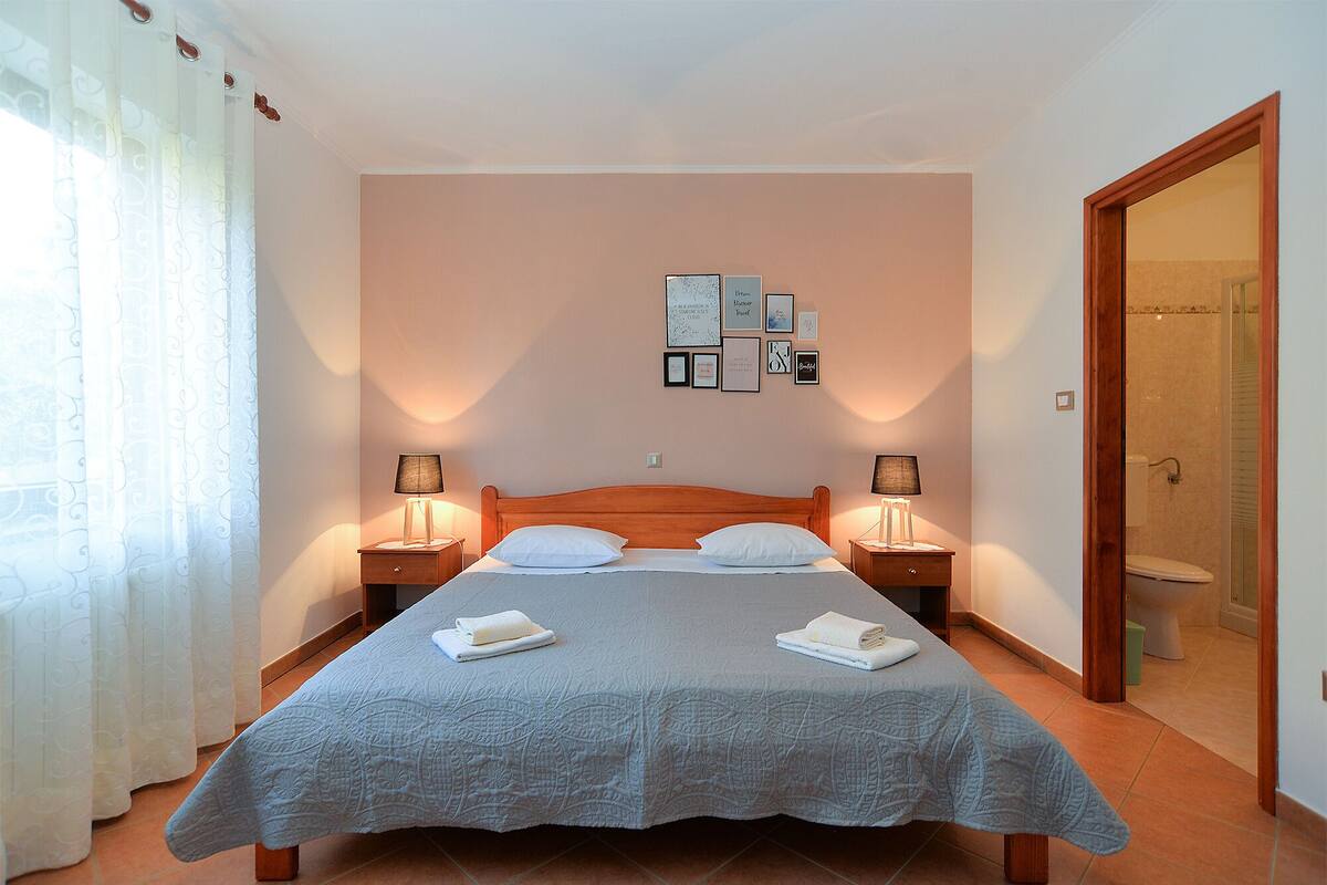 Ein Schlafzimmer mit Bett, zwei Nachttischlampen, einer Wand mit gerahmten Bildern und einer Badezimmertür.