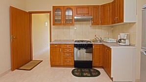 Een functionele keuken met houten kastjes, een gasfornuis, een oven, een koffiezetapparaat en een koelkast.