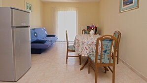 Een gezellig, compacte leefruimte met een kitchenette, een bank, een eettafel met bloemenkleed en twee stoelen.