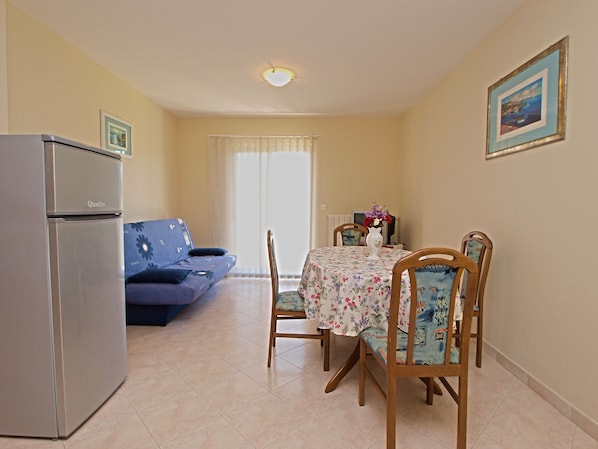 A compact living space with a kitchenette, a sofa, a dining table with floral tablecloth, and two chairs.