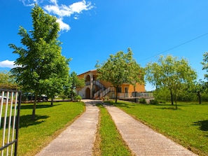 A pathway leading to a building with a stone facade and arched windows, surrounded by green grass and trees.