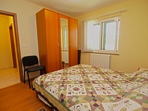 A bedroom with a bed, a chair, a wardrobe, and a window with blinds.