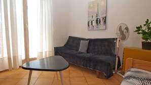 A living room with a sofa, a small table, a fan, and a painting of the Eiffel Tower. - Apartment 1095 (Pula)