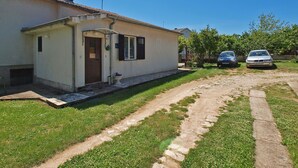 A single-story house with a tiled roof, a small front porch, and a paved driveway leading to a parked car. - Apartment 1095 (Pula)