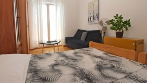 A bedroom with a bed, a small table, a sofa, a fan, a potted plant, and a painting on the wall. - Apartment 1095 (Pula)