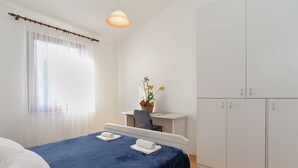 Een slaapkamer met een bed, een bureau, een stoel, een bloempot en een kledingkast.