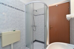 A bathroom with a glass-enclosed shower, a wooden door, and a white bathtub. - Apartment 1096 (Medulin)