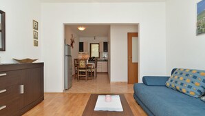 Een woonkamer met een blauwe bank, een houten salontafel en een eethoek met een tafel en stoelen.