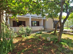 A building with a covered outdoor area, a tree, and a garden with plants and a small pond.