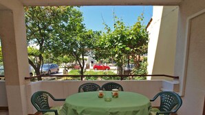 Un patio couvert avec une table ronde et des chaises, d’où l’on peut voir des voitures garées et des arbres au loin.
