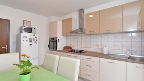 Une cuisine compacte équipée d’un four à micro-ondes, d’un four traditionnel et d’une cuisinière à gaz. On y trouve une table à manger avec des chaises et une plante en pot.