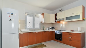 A modern kitchen with wooden cabinets, a white refrigerator, a microwave, a stove, and a sink. - Apartment 1100 (Pula)