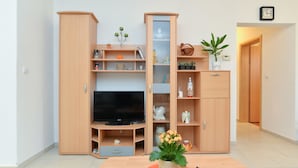 A modern living room with a flat-screen TV, wooden cabinets, and a dining table with a potted plant. - Apartment 1100 (Pula)