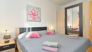 A modern bedroom with a large bed, a nightstand, a lamp, a mirror, and a painting on the wall. - Apartment 1100 (Pula)