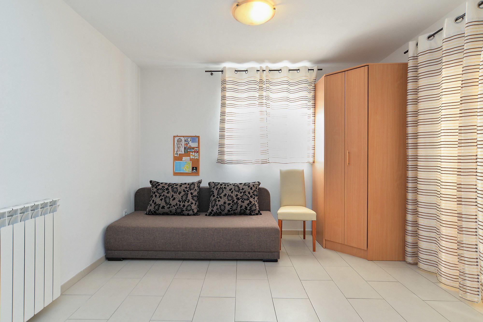 Ein kompakter Wohnraum mit Sofa, Stuhl, einem Holzschrank und einer Pinnwand.