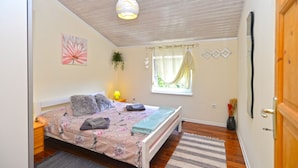 A bedroom with a bed, a window with curtains, a hanging plant, and a door. - Apartment 1113 (Fazana)