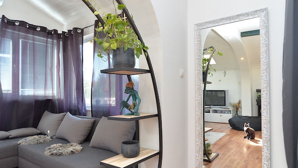 A modern living room with a grey sofa, a black plant shelf, and a large mirror. - Apartment 1113 (Fazana)