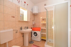 A bathroom with a sink, toilet, washing machine, and a glass shower enclosure.