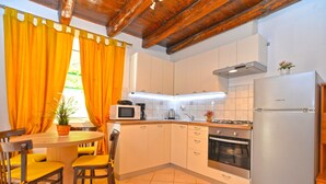 A compact kitchen with a dining area, featuring a wooden ceiling, white cabinets, a stainless steel refrigerator, and a microwave. - Apartment 1122 (Liznjan)