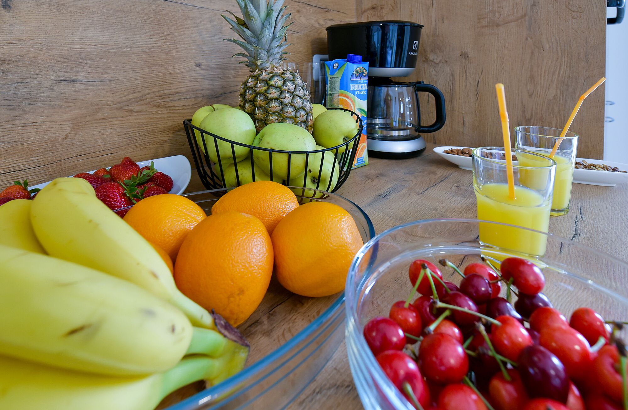 Ein Esstisch mit Früchten, einer Kaffeemaschine und Gläsern Saft.