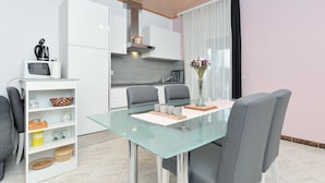 Cozinha moderna com armários brancos, micro-ondas e chaleira no balcão. Há uma mesa de jantar com cadeiras e um vaso com flores.