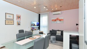 Uma sala de estar moderna com uma mesa de jantar de vidro, sofás cinza e uma televisão na parede.