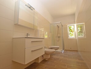 Et moderne badeværelse med en glasafskærmet brusekabine, toilet og en vaskebord med skuffer.