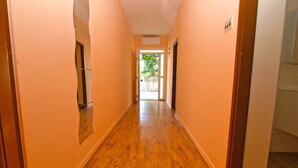 A hallway with wooden flooring and peach-colored walls, leading to a glass door that opens to a garden. - Apartment 1157 (Pula)