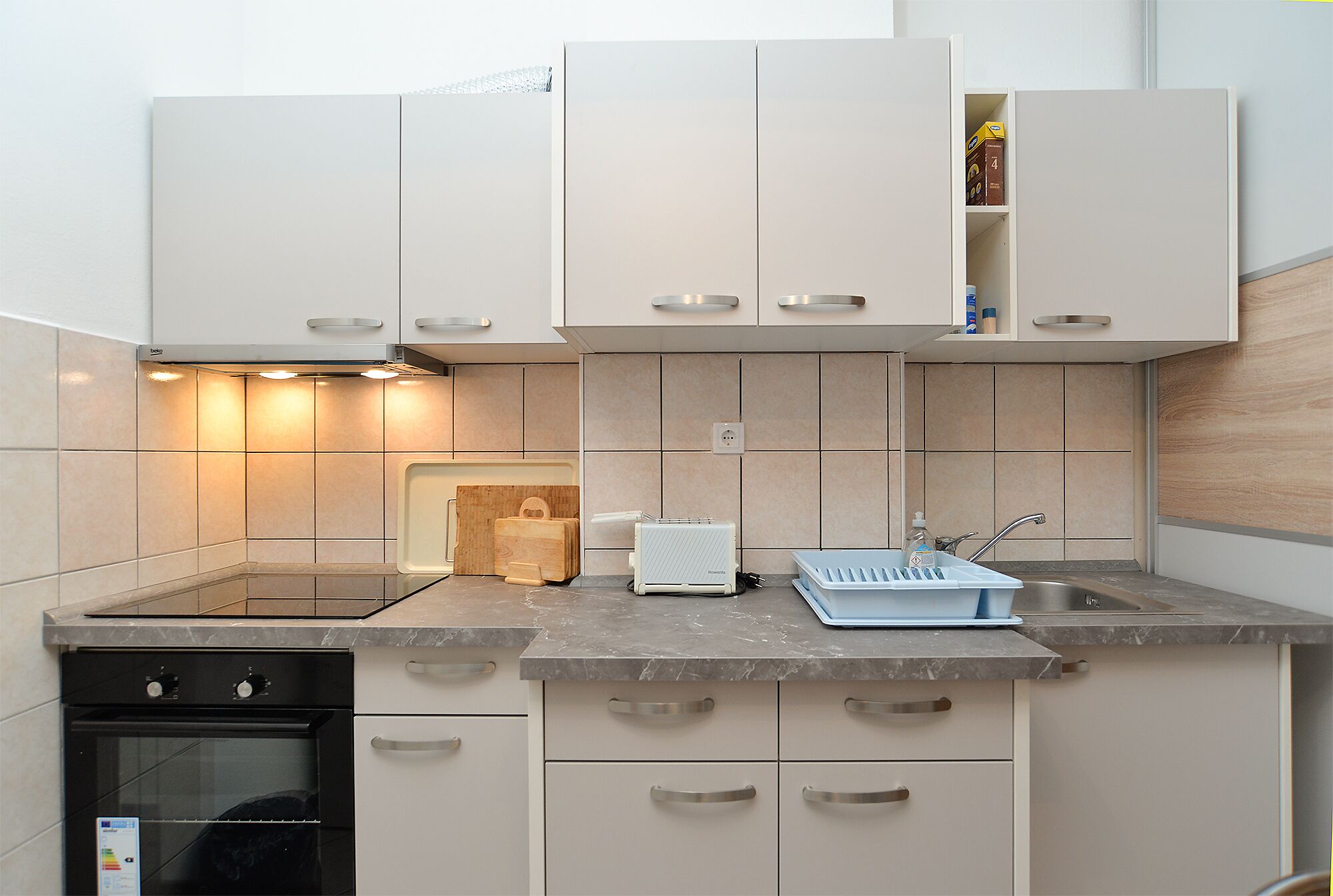 A modern kitchen with white cabinets, a built-in oven, a toaster, and a sink.