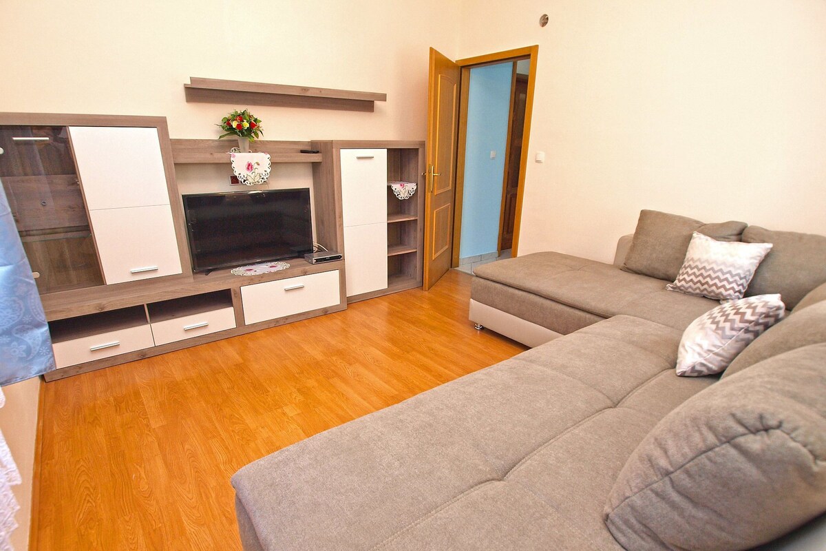 A modern living room with a grey sofa, wooden flooring, a flat-screen TV, and built-in cabinets.