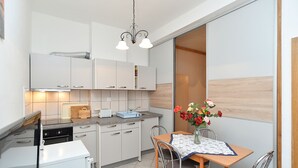 Een kleine keuken met witte kasten, een inbouwoven en een eethoek met een tafel en stoelen.