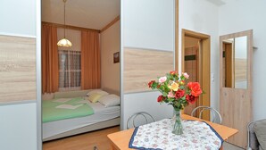 Een kleine kamer met een bed, een eettafel met een bloemrijk tafelkleed en een bloemenvaas.